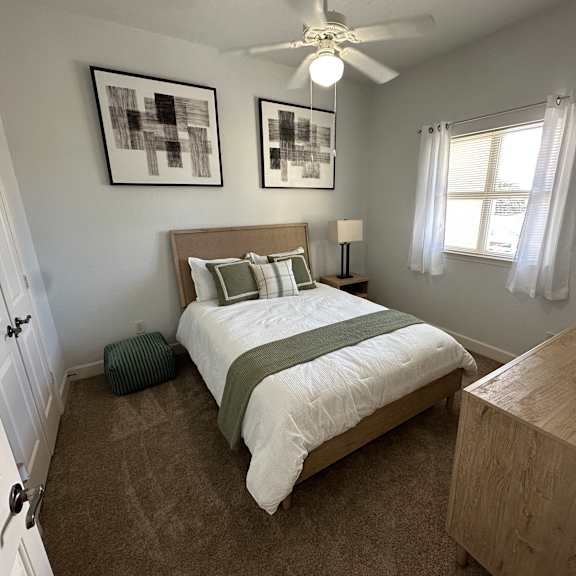 A bedroom with a bed, nightstand, and two pictures on the wall.