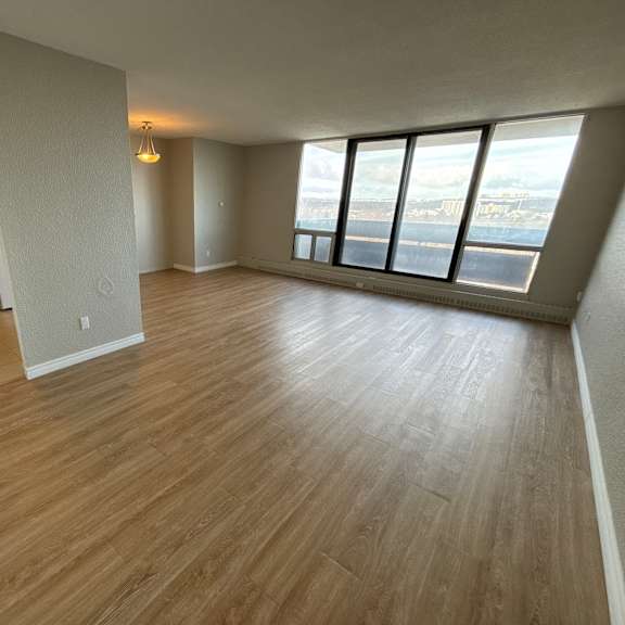 A room with wooden flooring and a large window overlooking a cityscape.