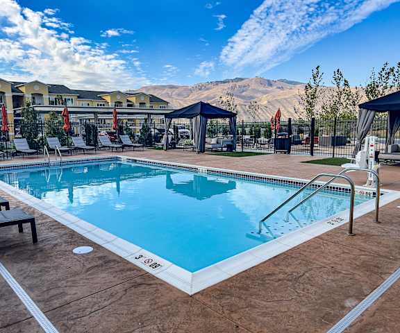 The turquoise outdoor pool with pool chairs, tables, and chairs with the apartments and mountains in the background at LIVEasy Street Apartments. 