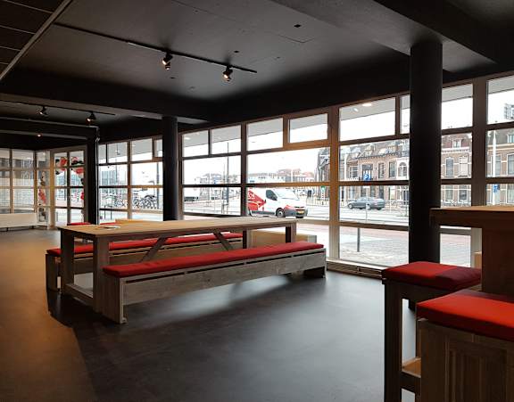 A long wooden bench with red cushions sits in a room with large windows.