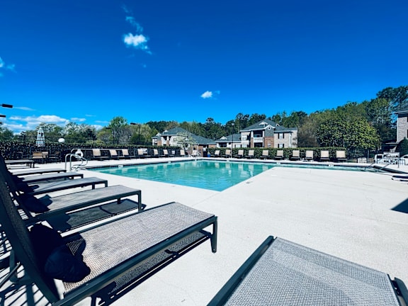 A pool with sun loungers and a building in the background.