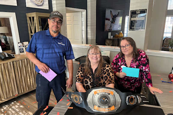 Three people are standing behind a table with a championship belt on it.