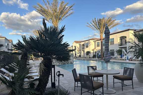 A poolside table with chairs and a palm tree. at Stella Luxury Apartment Homes in San Tan Valley, AZ