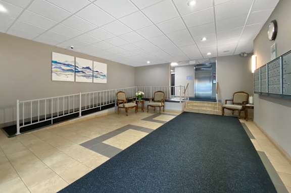 A hallway with a blue rug and chairs on the right side.
