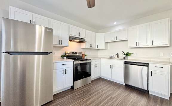 A modern kitchen with a stainless steel refrigerator and wooden flooring.