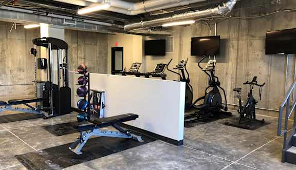 A gym with a variety of equipment including a bench, weights, and a television.