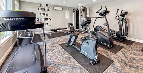 A gym with a treadmill, elliptical machines, and a wall with motivational words.