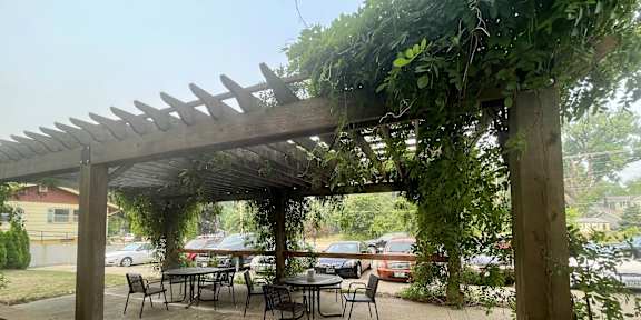 A wooden pergola with green vines growing on it is situated over a patio table.