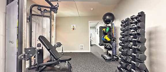 A gym with a variety of equipment including a weight bench, dumbbells, and a squat rack.