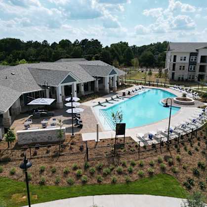 A large outdoor swimming pool surrounded by a black fence and a building in the background at The Crest at South Point Apartments, McDonough, GA, 30253