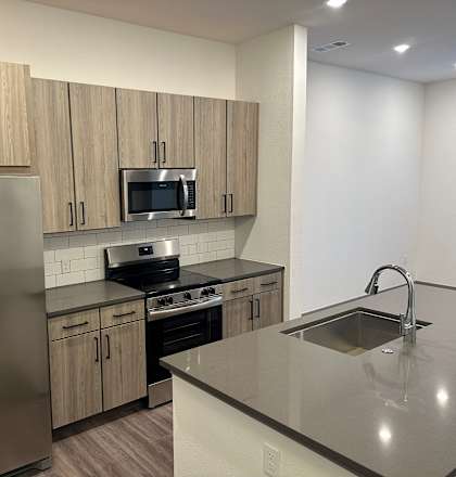 A kitchen with a refrigerator, microwave, oven, sink and cabinets.