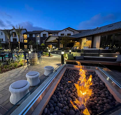 A fire pit in the middle of a patio surrounded by white ottomans at The Vineyards Apartments, California, 91326