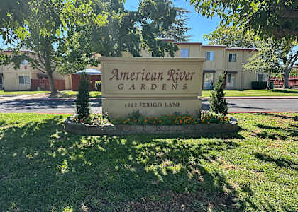 A sign for American River Gardens stands in front of a building.