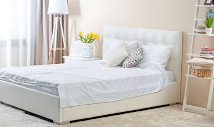 A white bed with a white headboard and a white nightstand with a lamp on it.