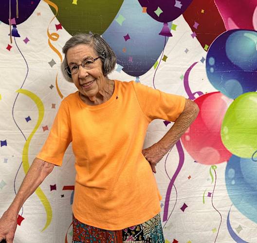 an older woman standing in front of a wall covered in balloons at Campus Commons Senior Living, Sacramento, CA 95825
