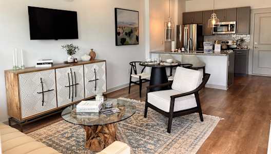 A modern living room with a wooden cabinet, a glass table, and a black chair.at Allier Gulf Shores, Gulf Shores, 36542