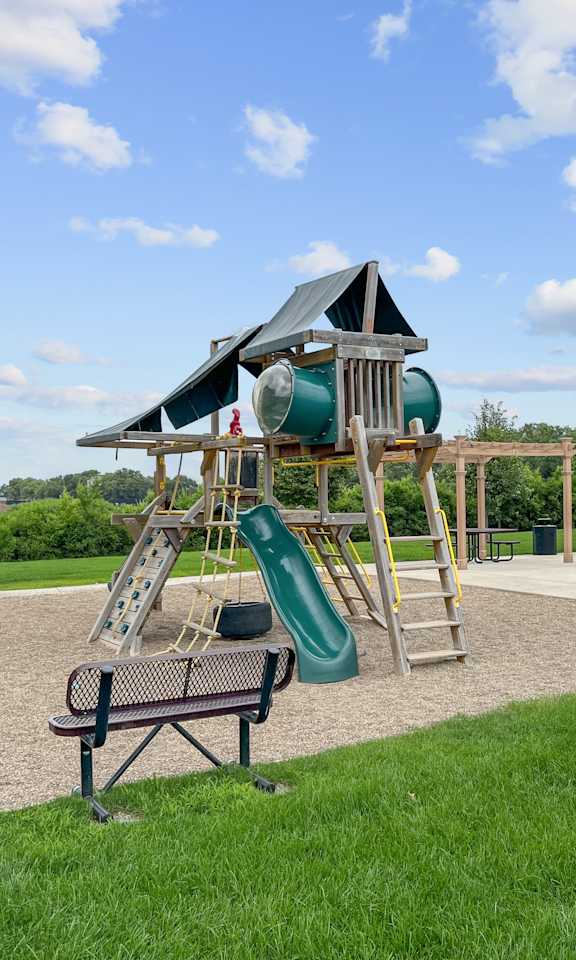 A playground with a green slide and a wooden swing set.
