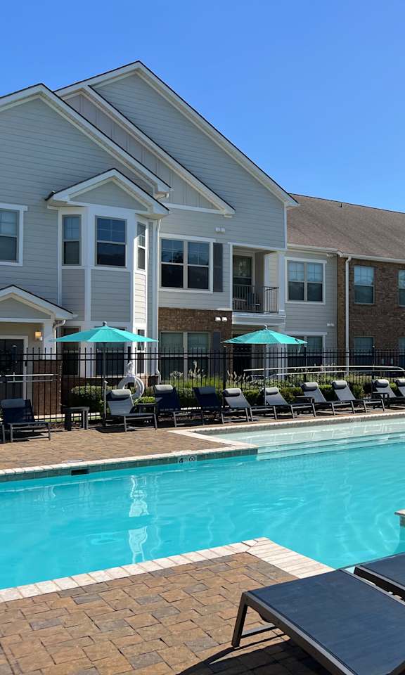 A pool area with lounge chairs and umbrellas in front of a building.