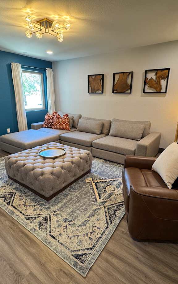 A living room with a grey couch, a grey armchair, a grey ottoman, a coffee table, a flat screen TV, and a painting on the wall.