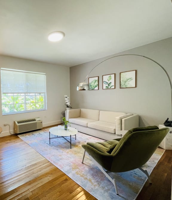 A living room with a white couch, a green chair, a round table with chairs, and a rug.
