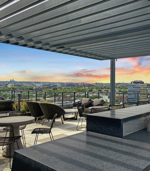 A rooftop patio with a grill and tables with chairs and a view of the Washington DC at Tribeca NOMA apartments