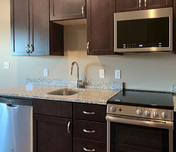 Kitchen with dark brown cabinets and matching stainless steel appliances in a studio apartment at the flats at shadow creek
