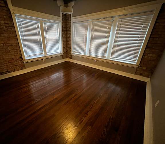 an empty living room with wood floors and a brick wall