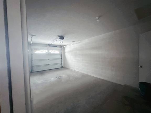 A room with a white ceiling and walls, a window with blinds, and a door on the right side.