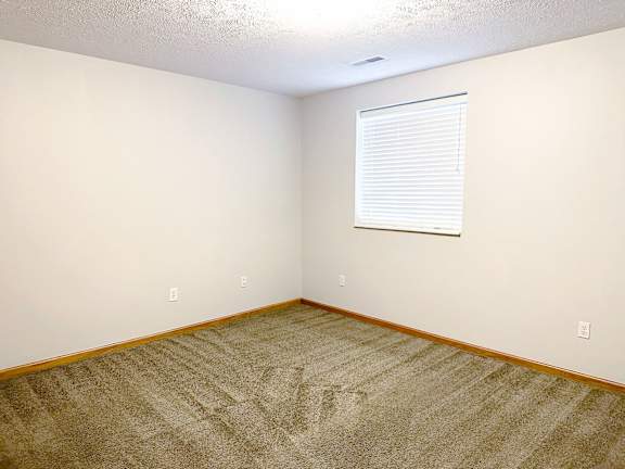 A room with a carpeted floor and a window with blinds.