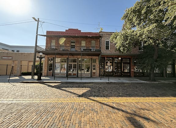 A sunny day in a town square with a red building and a cobblestone street.