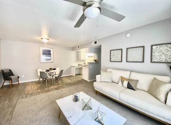 A living room with a white couch, a dining table, and a ceiling fan.