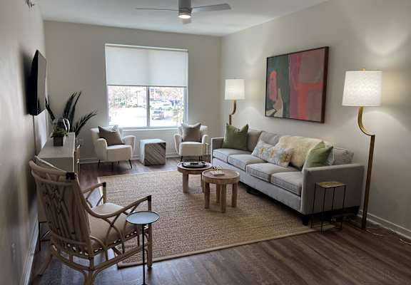 A living room with a grey couch, a wooden chair, a small table, and a painting on the wall.