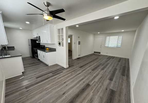 a renovated living room and kitchen with hardwood floors and a ceiling fan