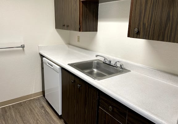 A white sink with a silver faucet is in a kitchen with brown cabinets.