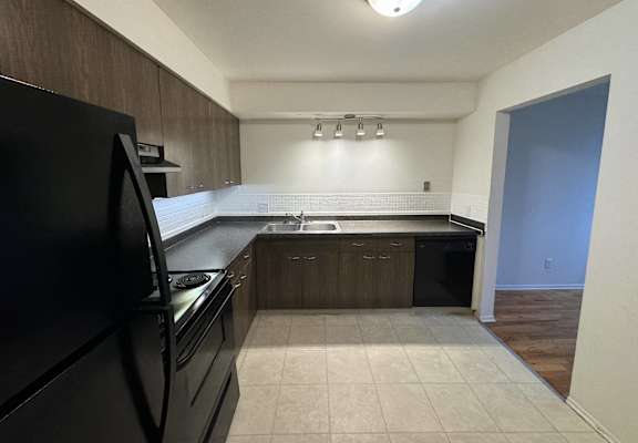 Kitchen with black appliances and wooden cabinets at Lodges Apartments
