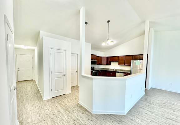 an empty living room and kitchen with white walls and wood flooring