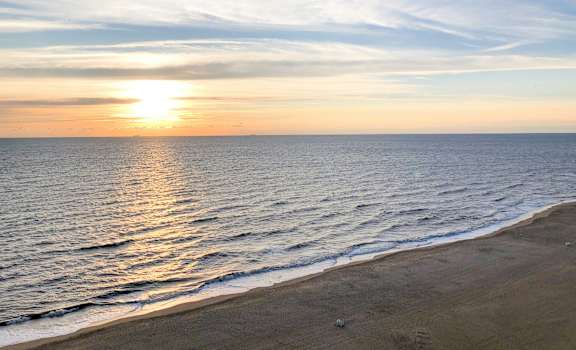 A beautiful beach scene with the sun setting over the ocean.
