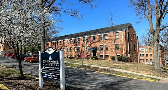 A sign for Cottage Square Apartments is in front of a brick building.