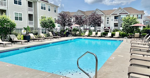 A swimming pool surrounded by lounge chairs and apartment buildings in the background.