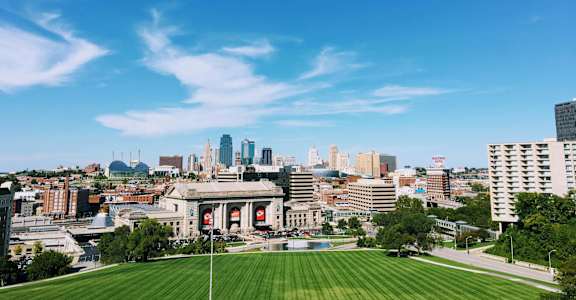 A cityscape with a large building in the center and a green field in the foreground.