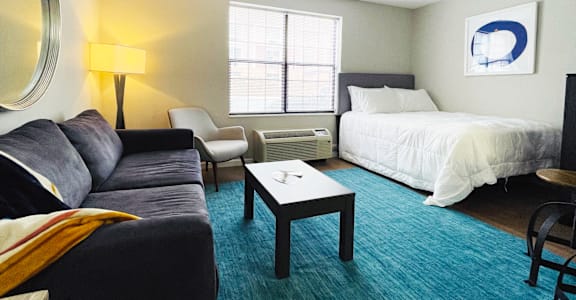 A well lit bedroom with a bed, chair, couch and a table.