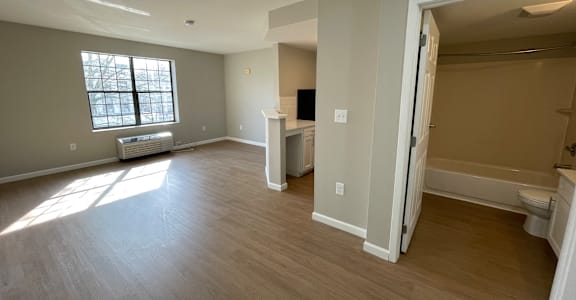 A large, empty room with a window and a door leading to another room.