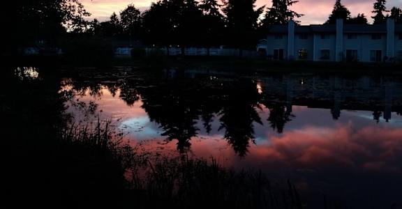 a sunset over a lake with trees and buildings in the background