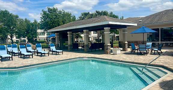 A large swimming pool with a pavilion and lounge chairs.