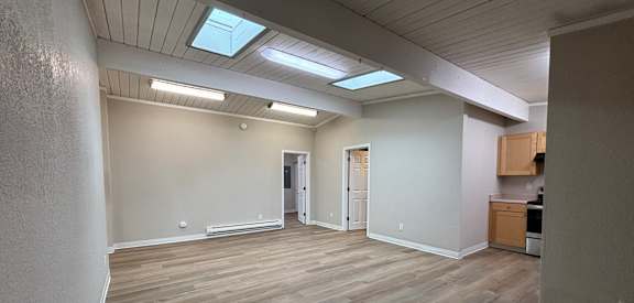 an empty living room with wood flooring and a kitchen
