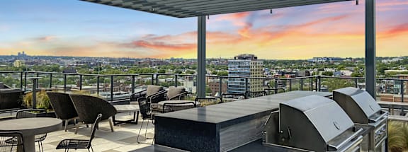 A rooftop patio with a grill and tables with chairs and a view of the Washington DC at Tribeca NOMA apartments