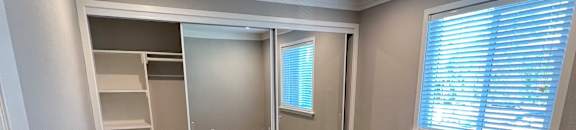 View of bedroom with carpet flooring, sliding mirror closet door with built in shelving, and well lit window