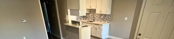 View into living area, dining area, and kitchen. Has recessed lighting, wood like flooring, and white cabinets.