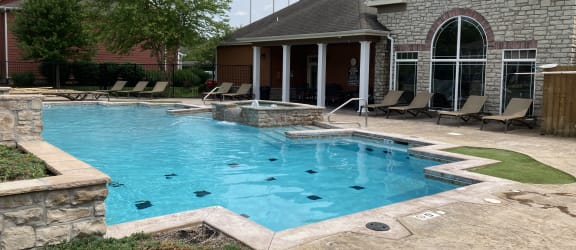 a large swimming pool with a stone wall and a patio with lounge chairs