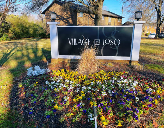a sign for village of lasso in front of a garden of flowers